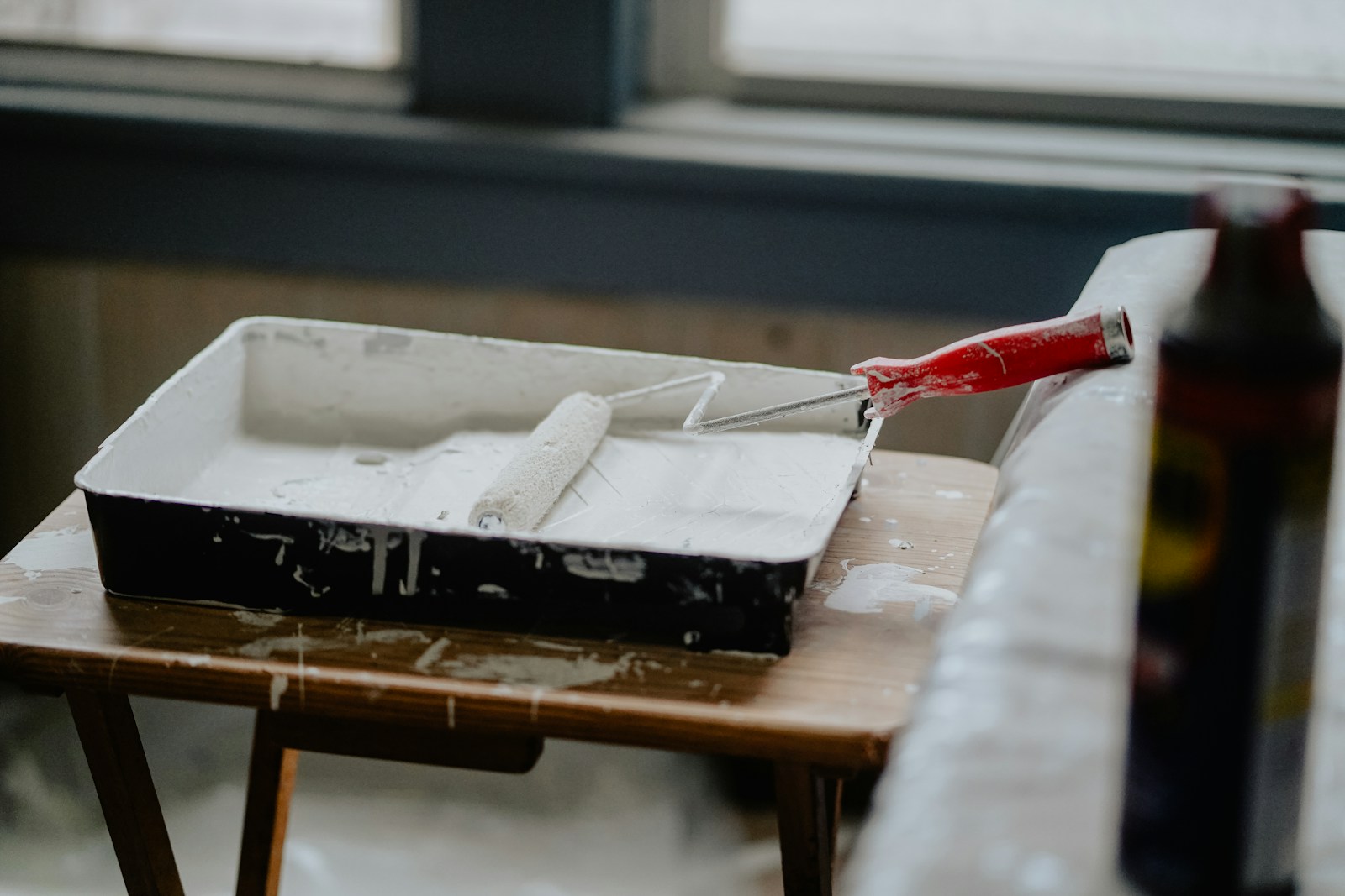 paint roller and tray with white paint in it on brown table
