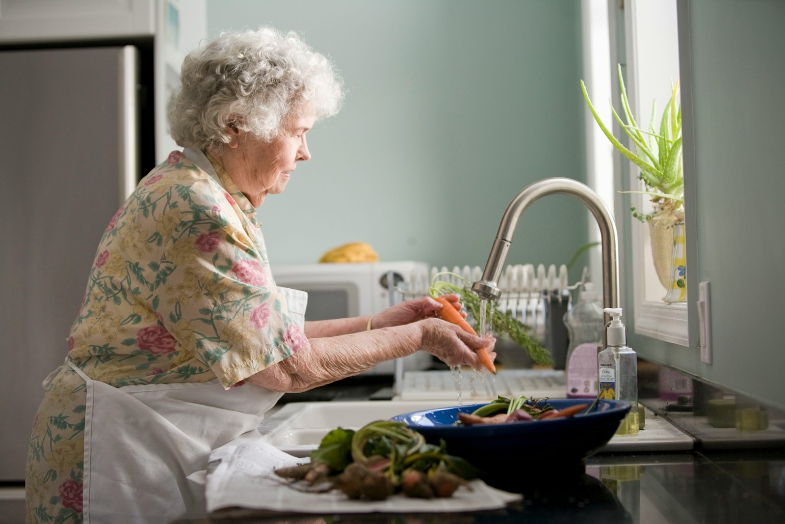 woman wearing yellow and pink floral dress washing carrots